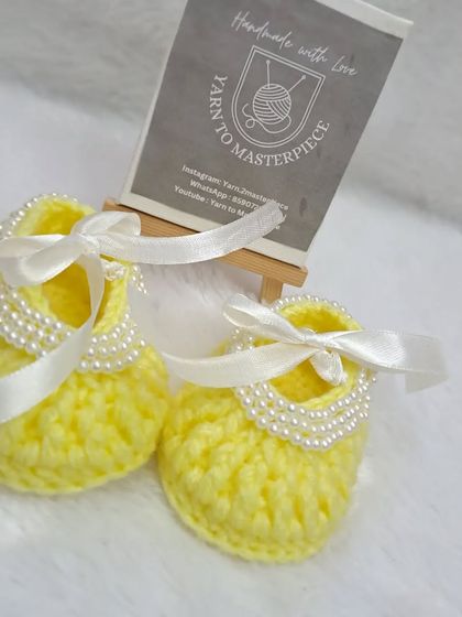 A close-up of the yellow pearl-studded booties, showing the delicate white ribbon and the neat line of pearls.