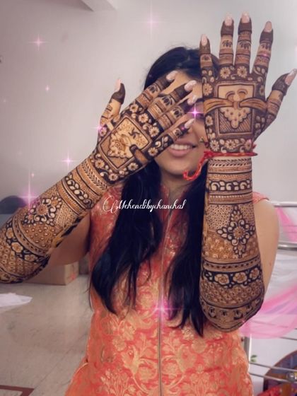 A happy bride peeking through her beautifully adorned hands. The intricate design covers her palms and fingers completely.