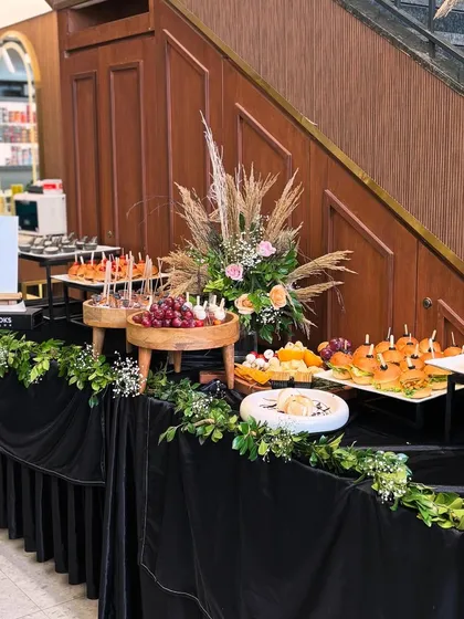 An elegant grazing table setup for a Looks Salon launch event. The display is styled with a dramatic black velvet cloth and lush greenery, featuring tiered platters of caprese skewers, mini burgers, and a curated cheese board.