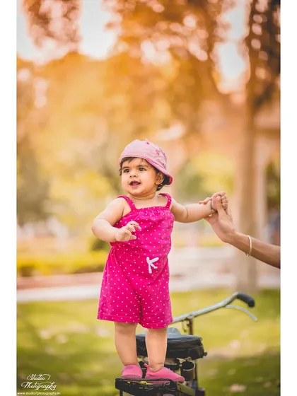 A vertical portrait from the same first birthday session, showing her standing tall with a little help. The warm, golden light of the park adds a beautiful glow to these milestone moments.