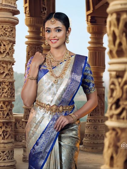 A smiling portrait of a model in a traditional South Indian bridal look. The background of intricately carved pillars adds a majestic feel to this beautiful and happy shot.