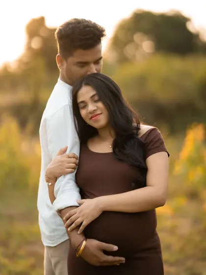 An intimate moment between an expecting couple, captured outdoors during golden hour. The warm light creates a romantic and gentle mood.