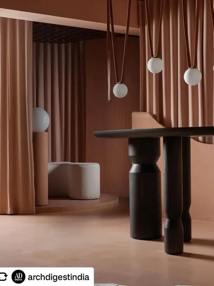 The strategic use of drapes allows the space to be flexible, creating partitions or revealing new areas. Here, they frame a view of hanging spherical lights and a custom-designed table.
