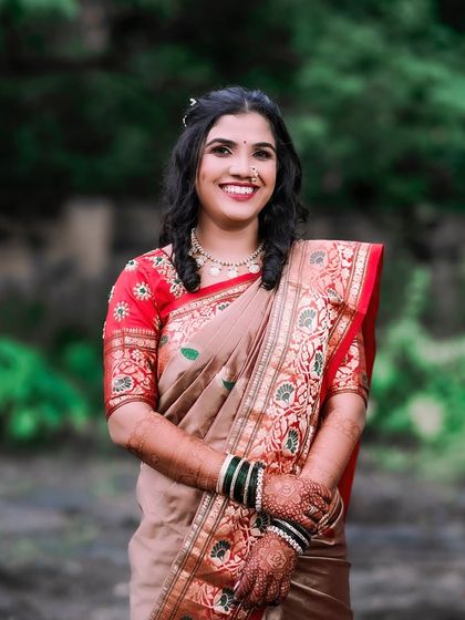 A beautiful outdoor bridal portrait. The bride is wearing a lovely Paithani saree, and her happy, relaxed smile is captured perfectly against the natural green background.