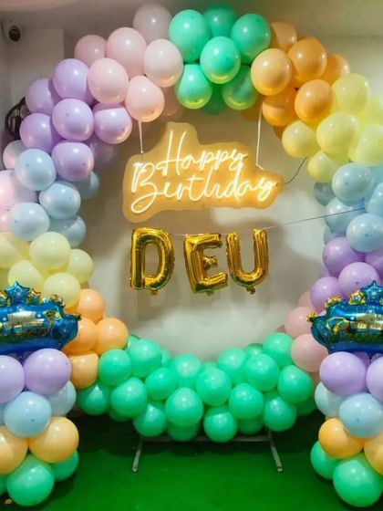 A rainbow pastel balloon ring backdrop for a personalized birthday celebration, featuring a neon sign and foil name balloons.