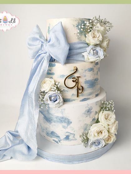 A dreamy wedding cake with a powder blue watercolor effect. This three-tiered beauty is adorned with white and blue roses and a large, flowing fabric bow.
