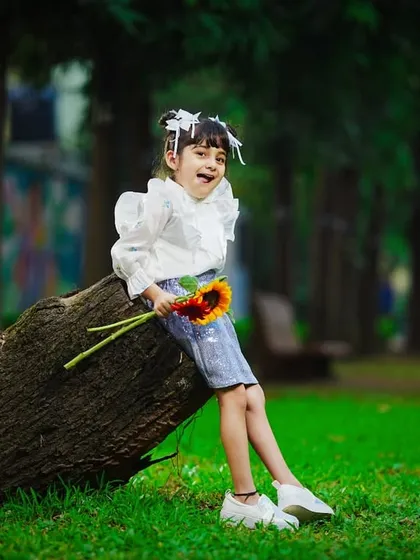 A sweet moment of rest, as the little girl sits on a log, holding sunflowers, with a beautiful green background.