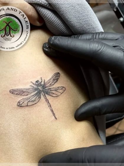 A tiny, single-needle dragonfly tattoo placed on the collarbone. This is an example of a delicate and subtle piece in a popular placement.