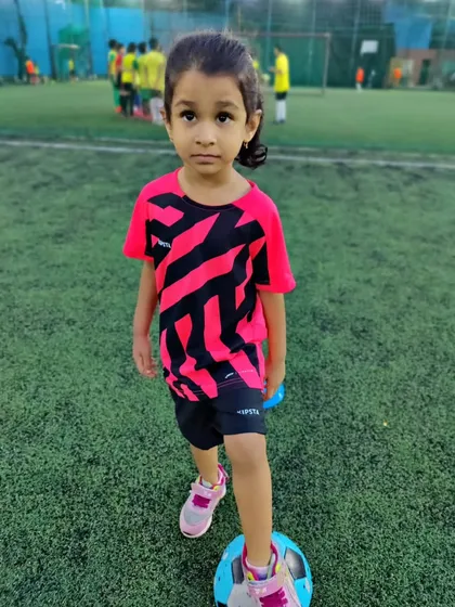 A young girl in our toddlers' program, looking focused with her foot on the ball. We are proud to have girls starting their football journey with us from a young age.
