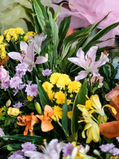 A close-up of the fresh flower mix, including lilies, chrysanthemums, and roses in a vibrant palette of yellow, orange, and pink.