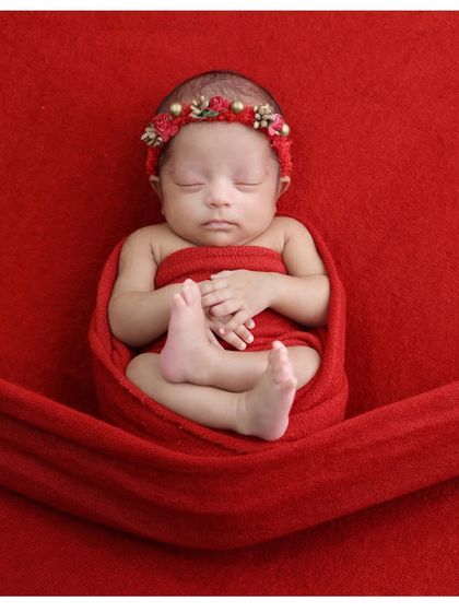 The classic "hands-under-chin" pose. This simple portrait on a red background beautifully showcases the baby's delicate features and tiny folded hands.