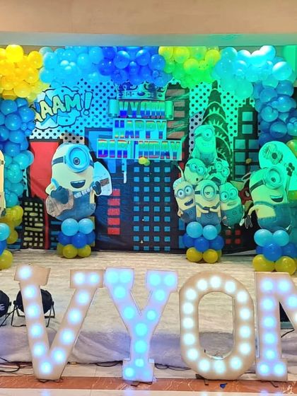 The Minions birthday stage with large, light-up marquee letters spelling the birthday boy's name, 'Vyom'. This is a great centerpiece for the party.