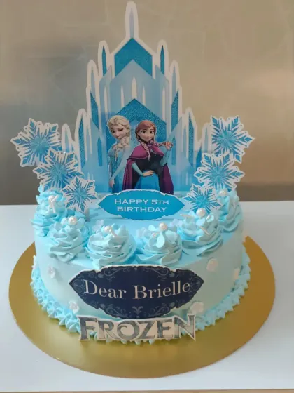 A magical "Frozen" themed cake for a 5th birthday. This blue cake is decorated with snowflakes and features an edible image of Elsa and Anna in front of their ice castle.