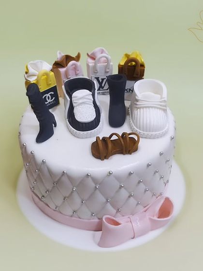 A fashion lover's dream cake, topped with a collection of miniature designer shoes, boots, and handbags from brands like Chanel and Louis Vuitton.
