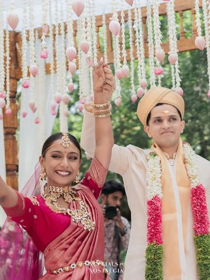 A triumphant moment as the newly married couple raises their hands in celebration under a beautiful floral mandap.