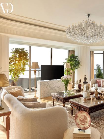 This living room is designed to maximize its stunning views, with floor-to-ceiling windows framing the panorama. The interior features a mix of classic and modern pieces, with a large crystal chandelier adding a touch of glamour.