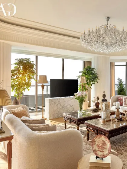 This living room is designed to maximize its stunning views, with floor-to-ceiling windows framing the panorama. The interior features a mix of classic and modern pieces, with a large crystal chandelier adding a touch of glamour.