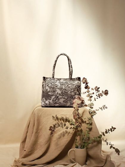 An elegant, vintage-inspired shot of a floral tote bag. The soft lighting, linen fabric, and dried flowers create a gentle, romantic mood.