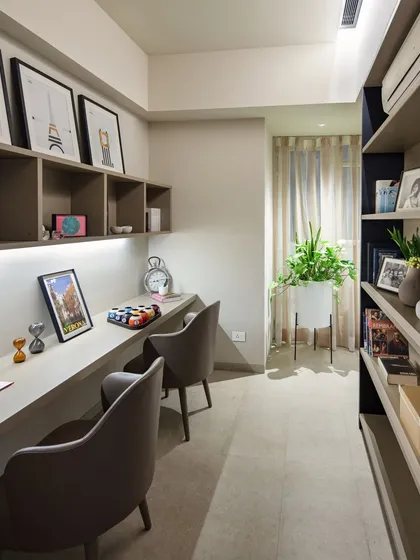 A long, built-in desk provides a functional workspace for two. Under-cabinet lighting ensures the area is well-lit, while the open shelving and deep bookshelf offer ample storage, keeping the desk surface clear and organized.