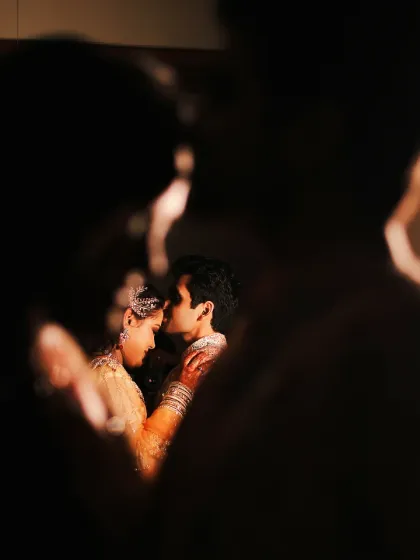 An artistic and intimate couple portrait. The couple is framed by the silhouettes of other people, creating a feeling that they are in their own world, lost in a private moment.
