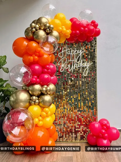 A vibrant sunset-colored balloon column against a multi-toned gold and orange shimmer wall. The clear bubble balloons add a modern and playful touch.