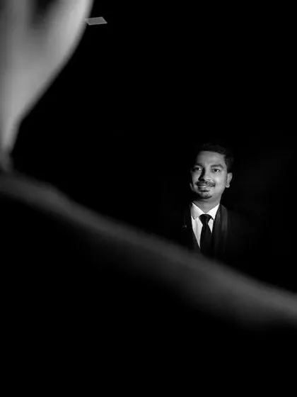 The groom's story is just as important. We captured this creative black and white portrait of the groom through a reflection, using the surrounding darkness to frame his confident smile as he awaits the ceremony.