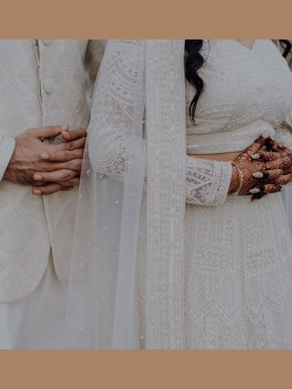 A detailed shot of the couple's hands and coordinated white outfits, focusing on the texture and artistry of their attire.