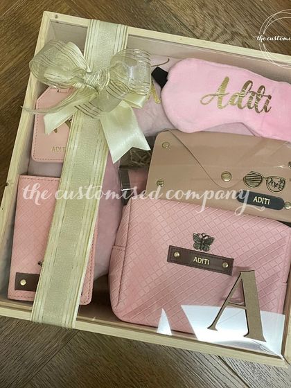 A personalized Rakhi gift hamper perfect for a sister who loves to travel. This set includes a variety of custom pink travel accessories, all beautifully arranged in a wooden crate.