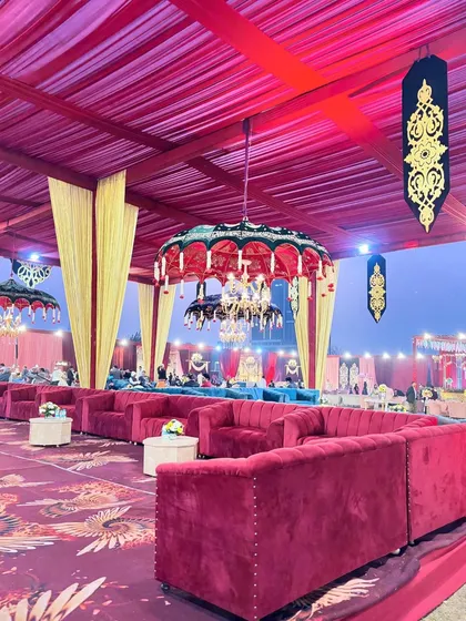 A luxurious lounge setup with deep red sofas, accented by teal couches and decorative umbrella chandeliers for a pop of color.