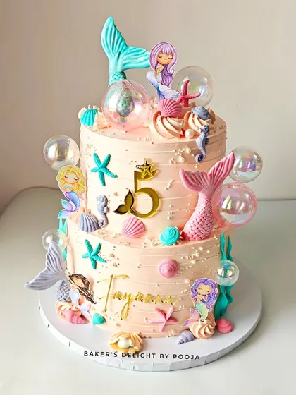 Dive into a magical underwater world with this two-tiered mermaid cake. Designed for a fifth birthday, it's decorated with pastel seashells, shimmering mermaid tails, and delicate bubble details, all crafted from whipped cream and fondant.