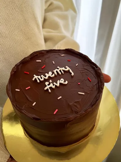 A minimalist 5-inch chocolate cake for a 25th birthday. The cake is covered in dark chocolate ganache and has simple text with sprinkles.
