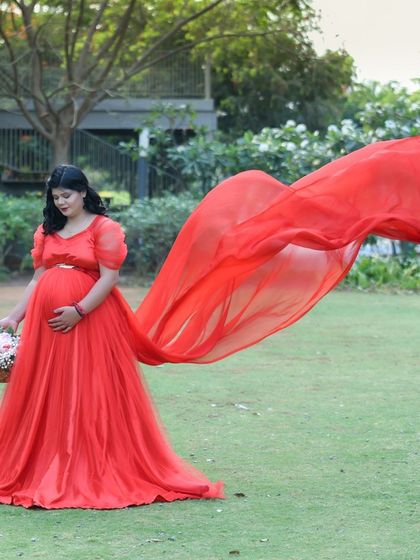 A beautiful, dynamic shot of a mom-to-be in a red gown with a long, flowing train, captured mid-air in a green park.