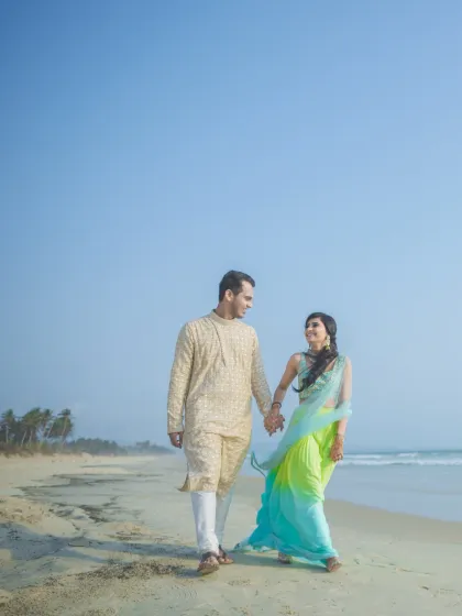 A serene pre-wedding photo of a couple walking on the beach, their colorful outfits contrasting beautifully with the blue sky and sea.