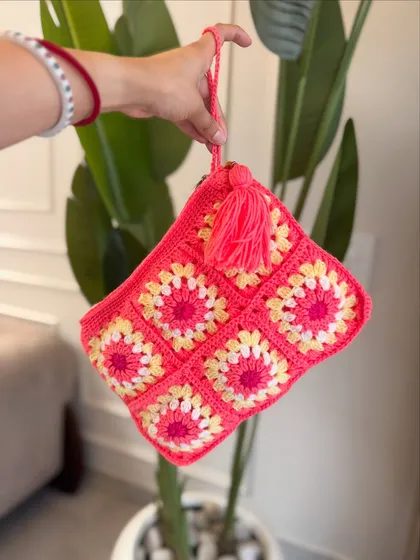 A styled shot of our pink granny square pouch. The tassel adds a fun, bohemian touch.