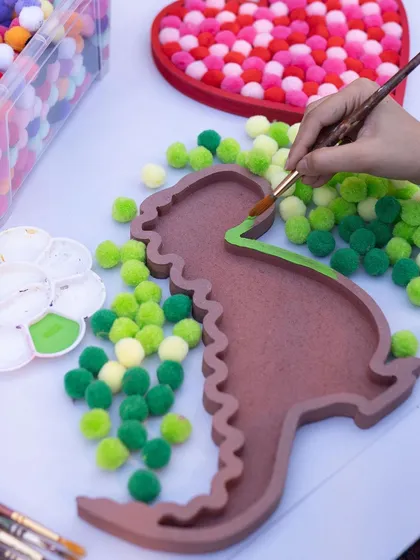 RAWR! This dinosaur-themed pom-pom art is one of our newest and cutest activities. Kids get to paint the wooden base and then fill it with soft, colorful pom-poms. It’s a fun sensory craft that looks great as room decor.