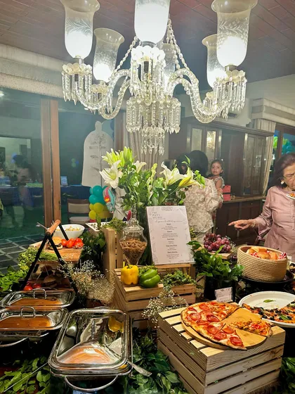 A wide view of a complete buffet setup in a client's home. You can see guests enjoying the spread, which includes hot dishes, salads, and fresh pizzas, all integrated into a beautiful tablescape.