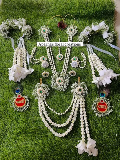 This is a complete baby shower floral jewellery set laid out to show all the pieces. It includes a necklace, earrings, maang tikka, kamarband, bajuband, and personalized 'Aai' and 'Baba' brooches.