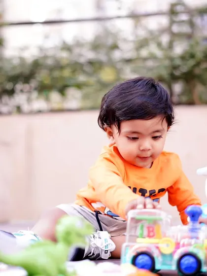 A candid moment of a toddler engrossed in playing with a toy train set during an outdoor session.