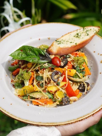 A beautiful plate of Aglio e Olio spaghetti, tossed with fresh vegetables, olives, and herbs, served with a side of garlic bread.