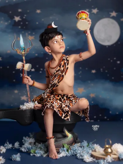 A young boy as Lord Shiva looks up at his damaru, with the moon and his trishul creating a powerful and atmospheric scene.