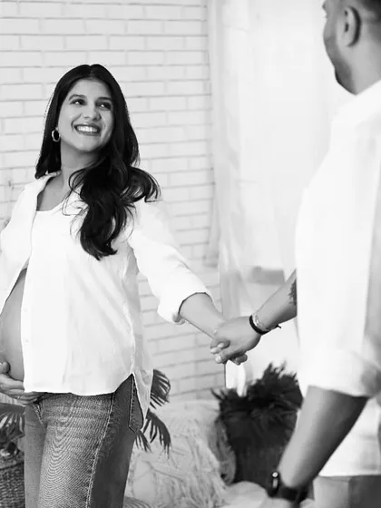 A candid black and white maternity photo capturing a beautiful smile from the mom-to-be as she holds her partner's hand.