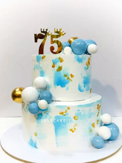 A simple and elegant cake for a 75th birthday. The light blue watercolor effect with gold and white spheres creates a modern and celebratory look.