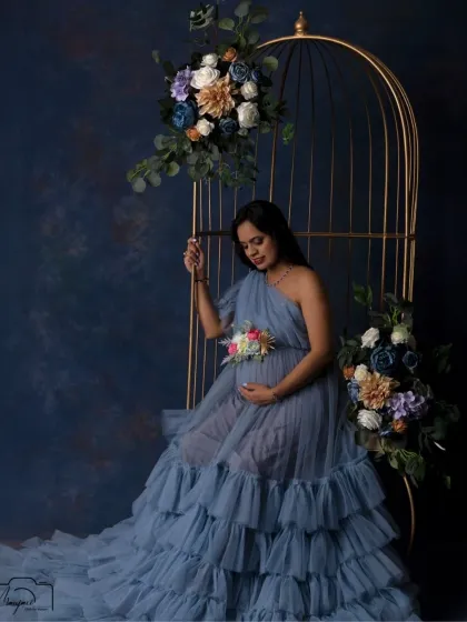 A moment of quiet reflection. Seated in the golden cage, this mama-to-be looks down at her bump with love, surrounded by dreamy pastel florals.