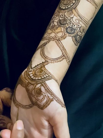 This design is created to look like a layered hathphool or hand harness. It features multiple bands and chains connecting the wrist to the fingers, all drawn with henna.