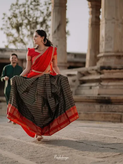 A bride-to-be walks with grace through a pillared corridor, her traditional half-saree adding a splash of color to the ancient architecture.