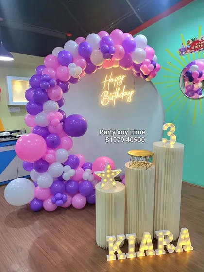 A fun 3rd birthday celebration for Kiara with a purple, pink, and white balloon arch. The setup includes a light-up number '3' and personalized name letters.