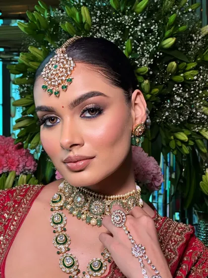A close-up on the details of a traditional red bridal look. The styling focuses on the kundan jewelry, including the maang tikka and hath phool.