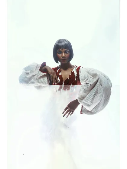 An experimental portrait using a translucent material to create a barrier between the model and the lens. The styling, with a sharp bob and textured top, is partially obscured, creating a sense of mystery.