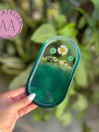 An oval-shaped trinket tray in a deep green, adorned with preserved daisies and gold leaf. Its simple, elegant design is perfect for minimalist decor.