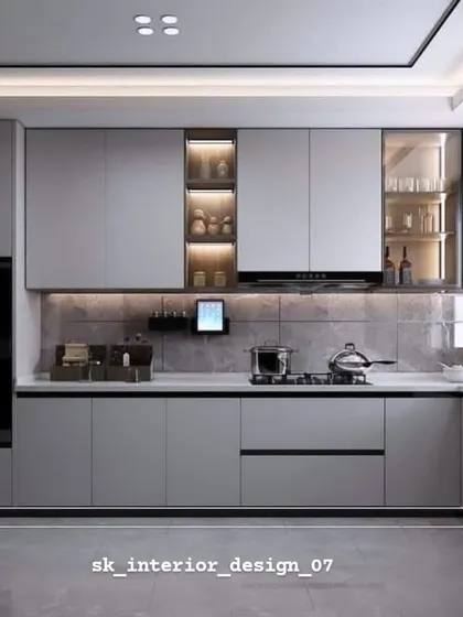A modern grey kitchen with integrated ovens and glass-fronted display cabinets. The small tablet holder on the wall is a smart touch for viewing recipes while cooking.